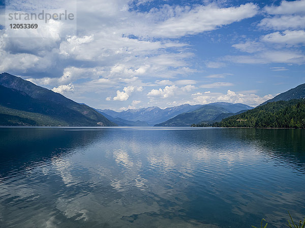 Der blaue Himmel und die Wolken spiegeln sich im ruhigen Wasser des Kootenay Lake in den Selkirk Mountains; Nelson  British Columbia  Kanada