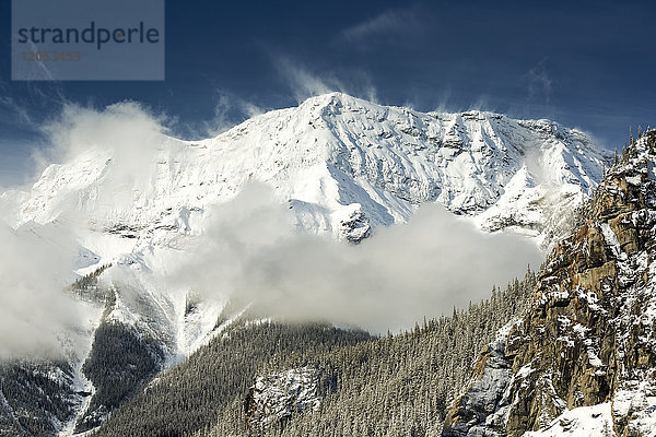 Schneebedeckter Berg mit Nebel und schneebedeckten Bäumen mit blauem Himmel; Alberta  Kanada