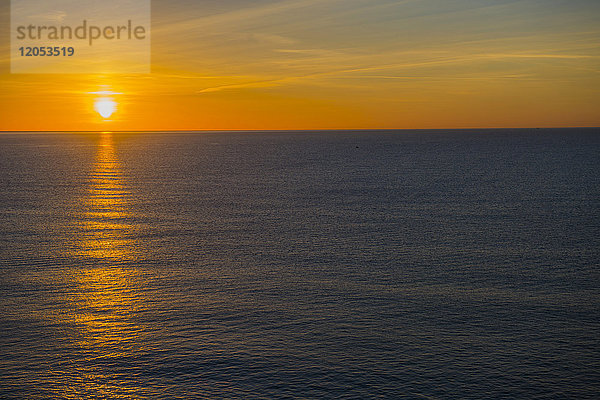 Die goldene untergehende Sonne beleuchtet den Horizont und spiegelt sich auf dem ruhigen Wasser des Ozeans; Menton  Cote d'azur  Frankreich