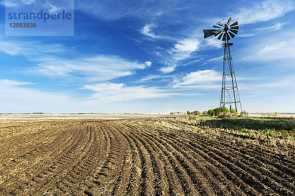 Eine alte Windmühle neben einem kürzlich bepflanzten Feld mit interessanten Wolken und blauem Himmel; Beiseker  Alberta  Kanada
