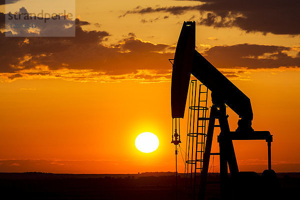 Silhouette eines Pump Jack bei Sonnenaufgang mit einer bunten Orange Sonne  Wolken und Himmel; Alberta  Kanada