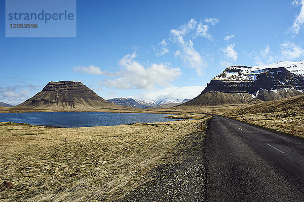 Eine Asphaltstraße entlang der Küste mit schneebedeckten Bergen  Halbinsel Snaefellsnes; Island