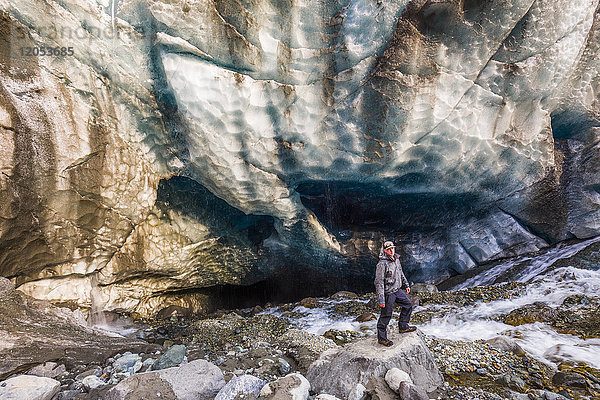Ein von rauschendem Wasser umgebener Mann posiert vor einer Höhle unter dem Eis des Root Glacier im Wrangell-St. Elias National Park; Alaska  Vereinigte Staaten von Amerika