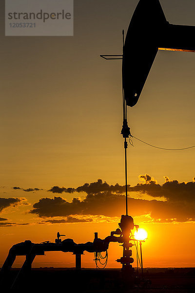 Silhouette eines Pumpjack und gut Kopf bei Sonnenaufgang mit einem bunten Orange Sonne  Wolken und Himmel; Alberta  Kanada