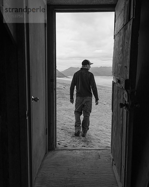 Ein Mann und das Valley of Ten Thousand Smokes (Tal der zehntausend Rauchschwaden)  eingerahmt vom Eingang einer der Baked Mountain Huts (Gebackene Berghütten) im Katmai National Park; Alaska  Vereinigte Staaten von Amerika