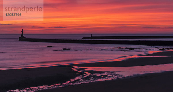 Silhouette eines Piers und eines Leuchtturms mit dramatischen und leuchtenden Farben des Sonnenaufgangs am Himmel  die sich im Meerwasser spiegeln; Sunderland  Tyne and Wear  England