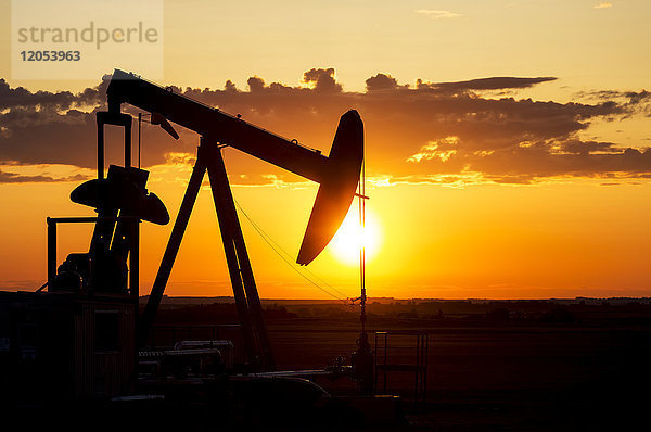 Silhouette eines Pump Jack bei Sonnenaufgang mit einer bunten Orange Sonne  Wolken und Himmel; Alberta  Kanada