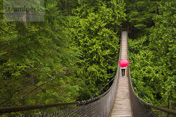 Frau mit einem roten  herzförmigen Regenschirm beim Überqueren der Lynn-Canyon-Hängebrücke  Nord-Vancouver; Vancouver  British Columbia  Kanada