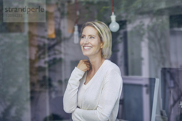 Porträt einer lachenden blonden Frau  die hinter einer Fensterscheibe steht