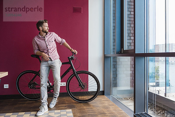 Mann mit Fahrrad stehend im modernen Büro mit Blick aus dem Fenster