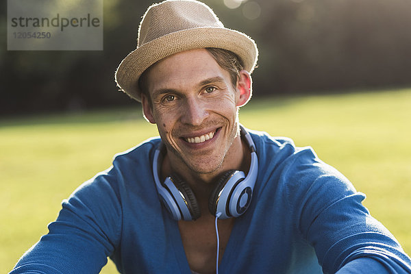 Porträt des lachenden Mannes mit Hut und Kopfhörer im Park