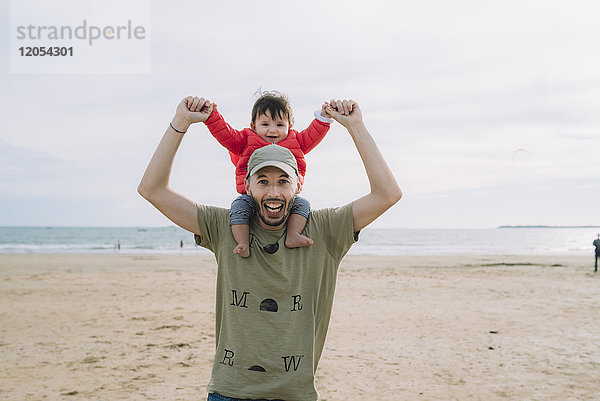 Porträt des Vaters  der seine kleine Tochter auf den Schultern am Strand trägt.