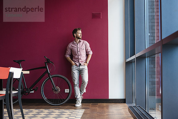 Mann mit Fahrrad stehend im modernen Büro mit Blick aus dem Fenster
