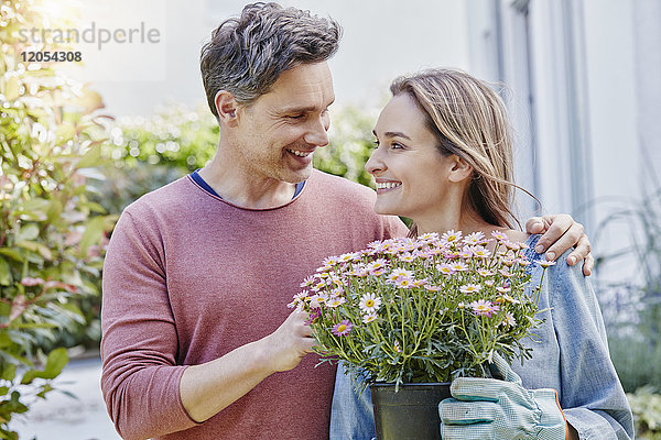 Lächelndes Paar mit Blumen vor dem Haus