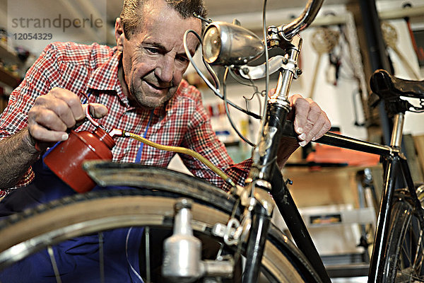Senior Mann beim Ölen von Fahrrädern in seiner Werkstatt