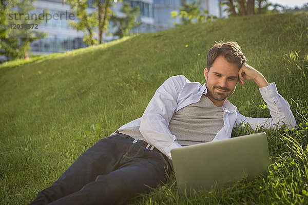 Mann auf Rasen liegend mit seinem Laptop
