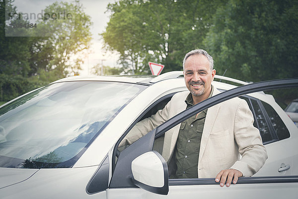 Porträt eines lächelnden reifen Geschäftsmannes beim Einsteigen in sein Auto