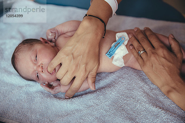 Neugeborenes Mädchen liegt auf einem Handtuch und saugt am Finger der Mutter.