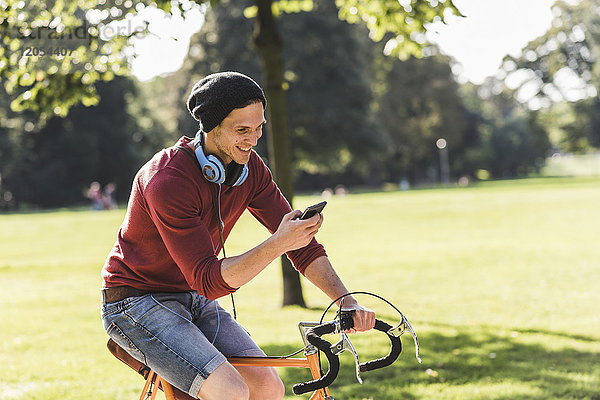 Lachender Mann auf dem Rennrad mit Blick auf das Handy im Park
