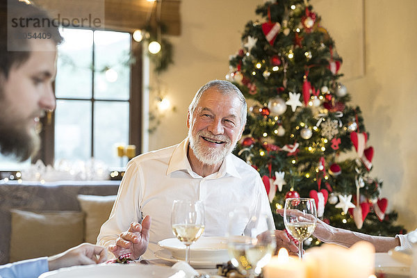 Lächelnder älterer Mann  der den erwachsenen Sohn am Weihnachtstisch ansieht.