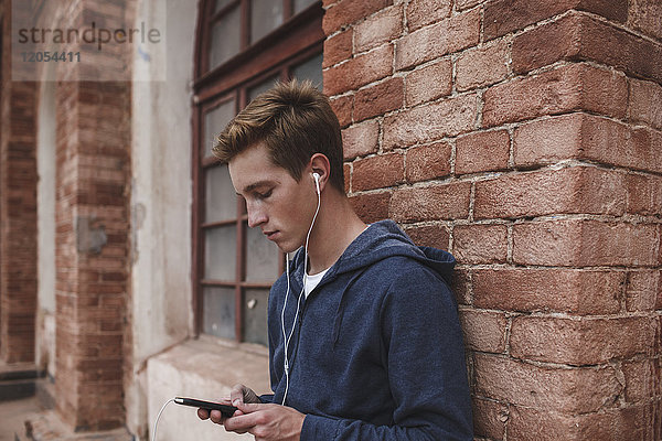 Junger Mann mit Handy und Kopfhörer im Backsteingebäude