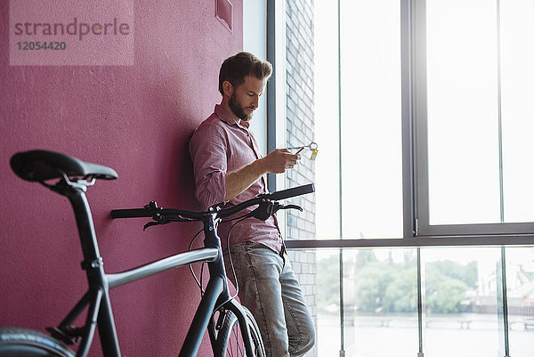 Mann mit Fahrrad im modernen Büro mit Blick auf das Handy