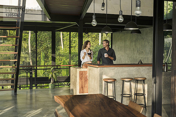 Paar beim Frühstücken und Lächeln in einer modernen Design-Küche mit Glasfassade  umgeben von einem üppigen tropischen Garten.