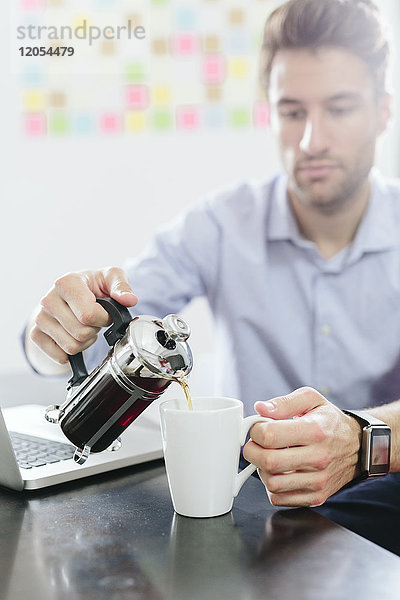 Junger Geschäftsmann am Schreibtisch mit Kaffeekanne