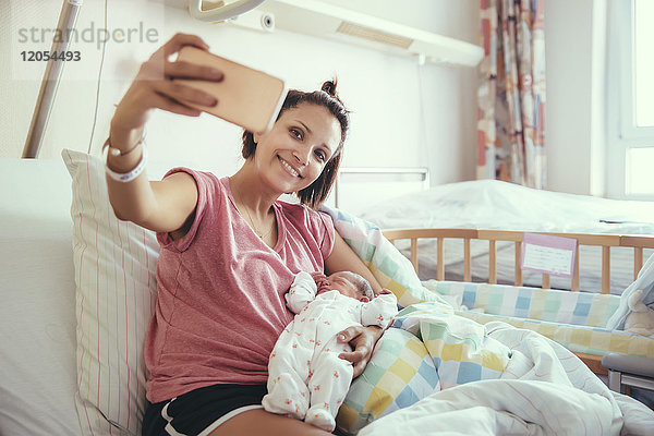 Mutter nimmt einen Selfie mit ihrem neugeborenen Baby im Krankenhausbett mit.