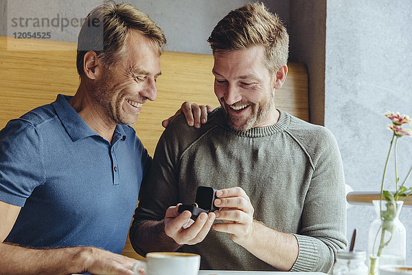 Aufgeregtes schwules Paar mit Ehering im Cafe