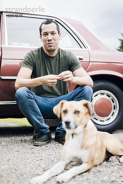 Porträt des lächelnden Mannes neben dem Auto mit Hund