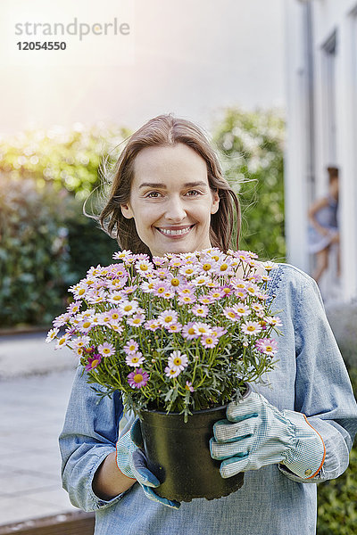 Porträt einer lächelnden Frau mit Blumentopf im Garten