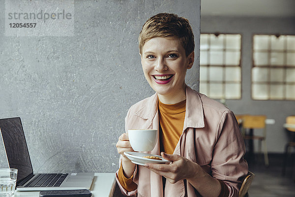 Porträt der lächelnden Frau im Café mit Laptop und Tasse Kaffee