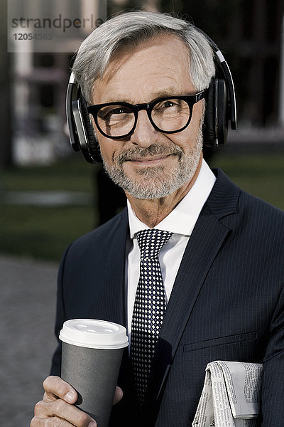 Grauhaariger Geschäftsmann mit Kopfhörer und Kaffee für den Blick in die Kamera