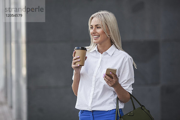 Glückliche Geschäftsfrau mit Kaffee zum Mitnehmen und Handy im Freien