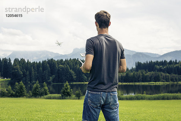 Deutschland  Bayern  Pfronten  junger Mann mit Drohne am Seeufer