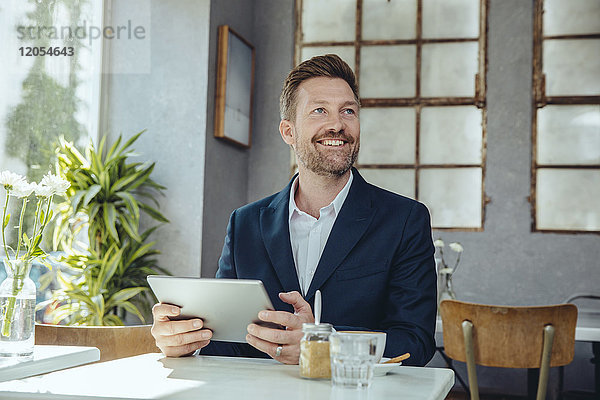 Lächelnder Geschäftsmann mit Tablette in einem Café  der nach oben schaut.