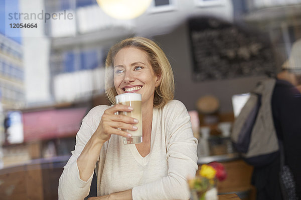 Porträt einer lächelnden Frau  die Latte Macchiato in einem Café trinkt.