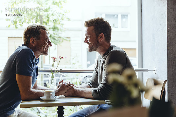 Schwules Paar hält sich im Cafe an den Händen und schaut sich gegenseitig an