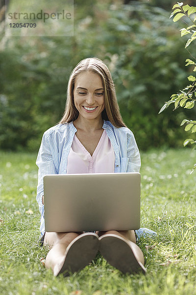 Lächelnde junge Frau mit Laptop auf der Wiese