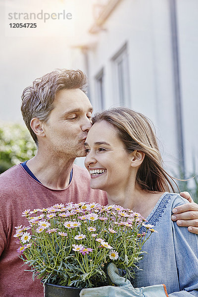 Mann küsst Frau mit Blumen vor ihrem Haus