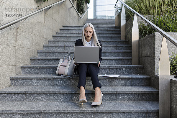 Junge Geschäftsfrau sitzend auf einer Treppe in der Stadt mit Laptop