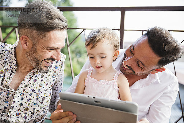 Glückliches schwules Paar mit Tochter auf dem Balkon mit digitalem Tablett
