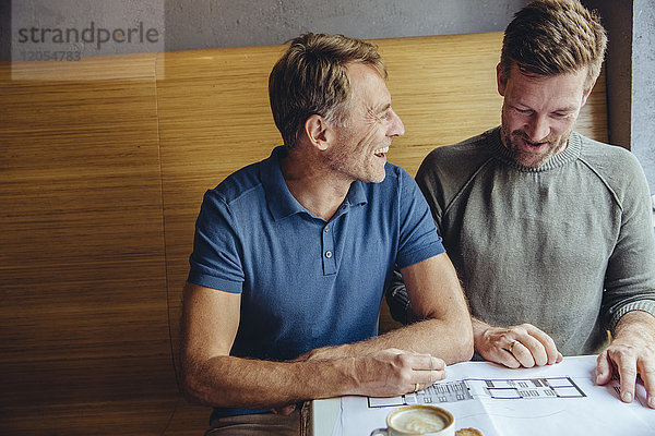 Glückliches schwules Paar  das sich Baupläne für sein Haus im Cafe ansieht.