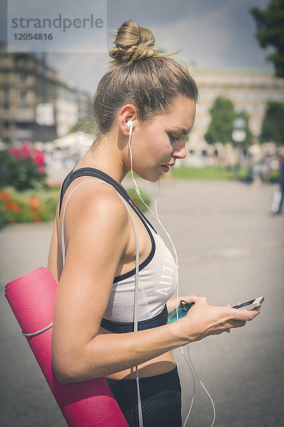 Junge Frau mit Yogamatte  Handy und Kopfhörer in der Stadt