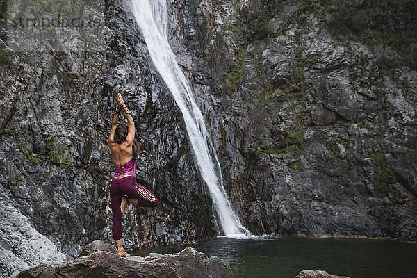 Italien  Lecco  Frau beim Tree Yoga Pose auf einem Felsen in der Nähe eines Wasserfalls
