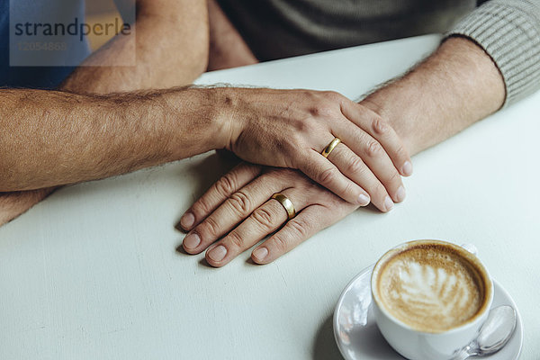 Nahaufnahme der Männerhände mit Eheringen und einer Tasse Kaffee