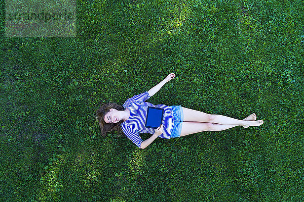 Junge Frau auf Gras liegend  mit digitaler Tafel