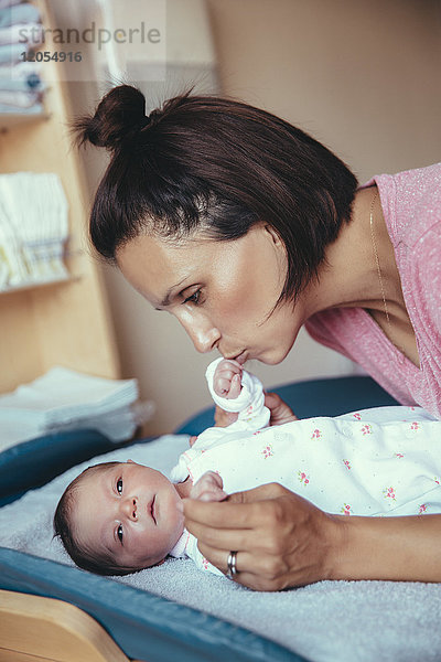 Mutter küsst die Hand ihres neugeborenen Mädchens im Krankenhauszimmer.