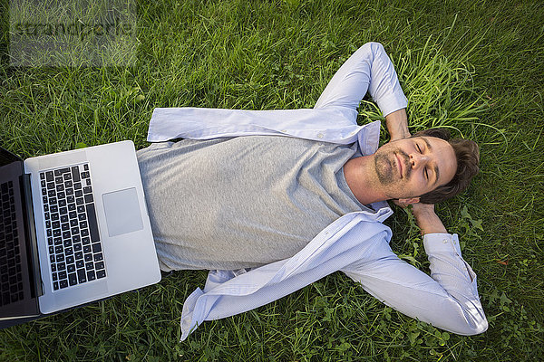 Mann entspannt sich im Sommer auf dem Rasen  mit Laptop am Bauch